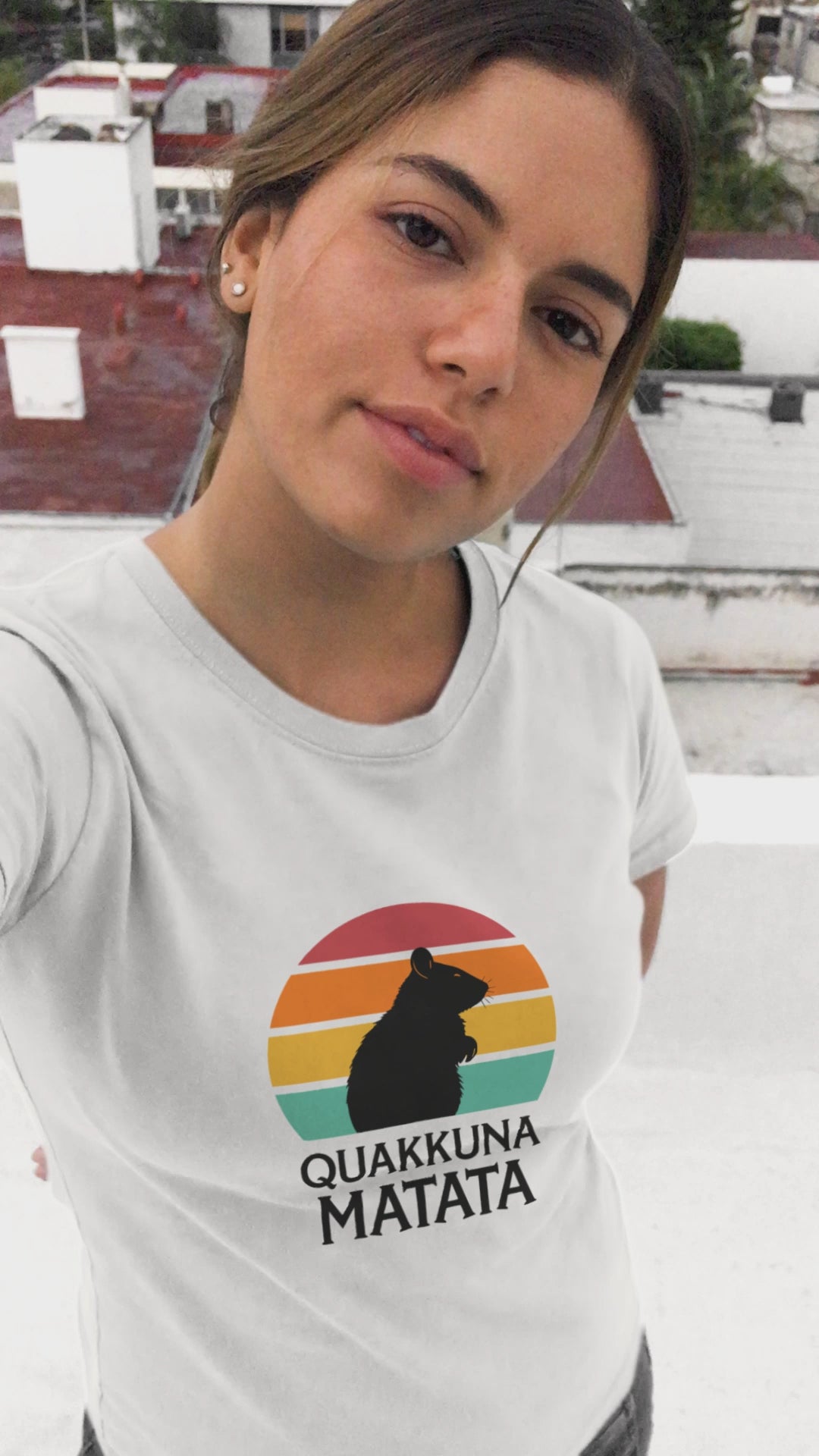 Young woman taking a selfie while wearing a white Quakkuna Matata T-shirt. Features a retro sunset design and quokka silhouette, inspired by Disney's Lion King Hakuna Matata.